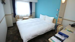 Ōtsukiにある東横INN富士山大月駅の白いベッドとデスクが備わるホテルルームです。
