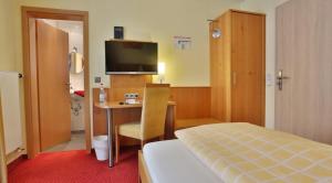 Habitación de hotel con cama y escritorio con TV. en Hotel KRONE Garni en Deckenpfronn