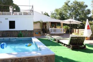 a pool with chairs and an umbrella next to a house at CHIBITEL Alojamiento Rural in Córdoba