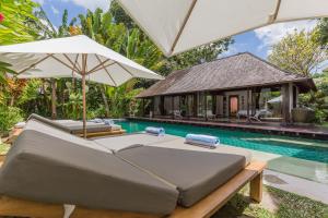 a bed with an umbrella next to a swimming pool at Bali Villa Home in Seminyak