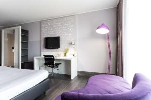 a bedroom with a bed and a desk and a purple chair at elaya hotel wolfenbuettel ehemals Rilano 24 7 Hotel Wolfenbüttel in Wolfenbüttel