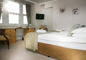 a bedroom with two beds and a desk and window at The Cumberland Hotel in Eastbourne