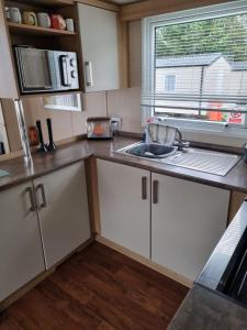 cocina con armarios blancos, fregadero y ventana en Beautiful 3 bed holiday home en Port Seton