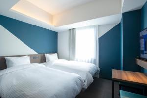 two beds in a room with blue walls and a window at Prince Smart Inn Hakata in Fukuoka