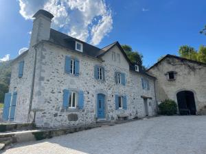 Arudy的住宿－Le Val Éveillé 4 étoiles - maison de maître de 1773，街上一座带蓝色百叶窗的古老石头建筑