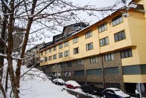 un grand bâtiment jaune avec des voitures garées dans la neige dans l'établissement Apartaments Del Meligar, à Encamp