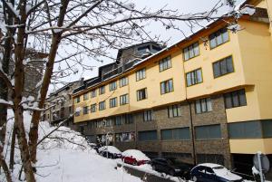 un grande edificio giallo con auto parcheggiate nella neve di Apartaments Del Meligar a Encamp