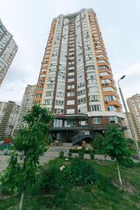 ein hohes Gebäude mit einem Park davor in der Unterkunft Apartment on Akhmatovoyi 32/18 in Kiew