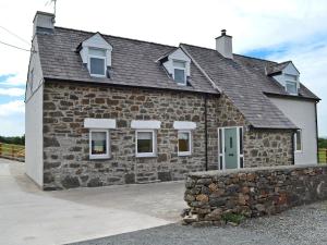 a stone house with a stone wall in front of it at Rhosydd Cottage in Llanerchymedd