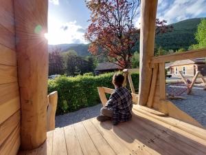 a man sitting on the porch of a wooden house at Le Valserine - Camping éco responsable in Chézery-Forens