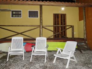 trzy białe krzesła siedzące przed budynkiem w obiekcie Vila do Surfe w mieście Ubatuba