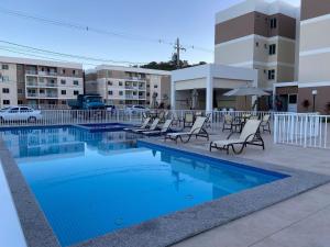 a swimming pool with chairs and an umbrella and buildings at Ilha Tenerife - Paraíso do Atlântico - Zona Sul in Ilhéus