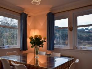 a dining room with a table and two windows at Dream Cottage in Strathyre