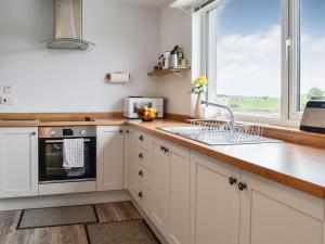 a kitchen with white cabinets and a sink and a window at High Threave Cottage in Kirkcowan