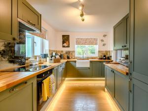 a large kitchen with green cabinets and wooden floors at Appledore Cottage in Farnham