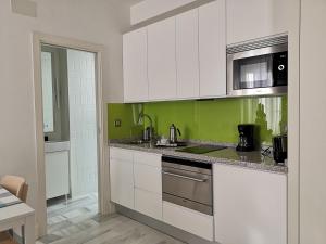White Loft Alameda في إشبيلية: مطبخ بدولاب بيضاء وجدار أخضر