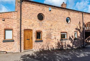 um edifício de tijolos com uma porta de madeira e janelas em No1 Little Barrow Barns - Sleeps 10 em Chester