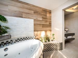 a bathroom with a white tub and a tile wall at ECO Villa Grand Karpatia Ski&Spa in Murzasichle