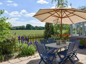 a table and chairs with an umbrella and a field at Hoggets Nest in Bedingfield