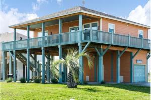a large orange house with a balcony and a palm tree at Fancy Nancy 2 Min Walk to Beach, Lyft, Pet-friendly in Bolivar Peninsula