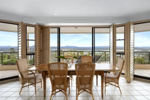 Un comedor con mesa y sillas y grandes ventanales. en Penthouse with Incredible Views & Pool, en Noosa Heads