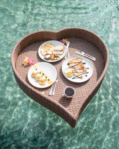 a heart shaped table with plates of food on the water at Rossa Garden Hotel in Candidasa