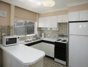 a kitchen with white cabinets and a white refrigerator at Beachpoint, Unit 101, 28 North Street in Forster