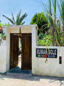 una pequeña casa con una puerta de madera y un cartel en Rumah DOLE en Gili Air