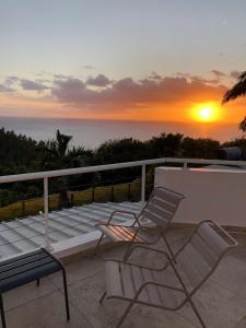 a bench and two chairs on a balcony with a sunset at Villa spa Grand Anse in Petite Île