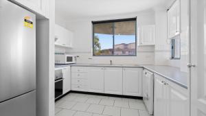 a white kitchen with white cabinets and a window at Ocean Palms Unit 2 in The Entrance