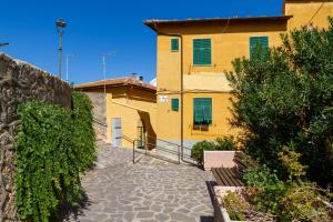 um edifício amarelo com persianas verdes numa rua em Casa la Fortezza em Porto Santo Stefano