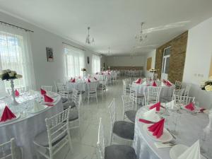 Cette chambre comprend des tables et des chaises blanches avec des serviettes rouges. dans l'établissement Pensiunea Adrian, à Novaci-Străini