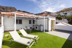 un patio trasero con césped verde y sillas blancas y una casa en Casa Isabela with Roque Nublo view, en Tejeda