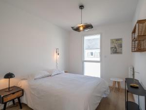 a white bedroom with a bed and a table and a window at Apartment Le Clos Moguer-2 by Interhome in Quiberon
