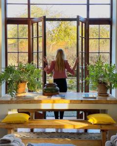 Eine Frau, die an einem Tisch steht und aus einem Fenster schaut. in der Unterkunft The Stable Yard House at Burtown House & Gardens in Athy