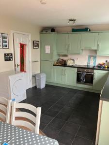 a kitchen with green cabinets and a black tile floor at Ballycastle, Strand Cottages Modern Home in Ballycastle