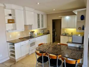 uma cozinha com armários brancos e uma mesa com cadeiras em Palm Zicht MAIN 3 bedroom apartment em Cidade do Cabo