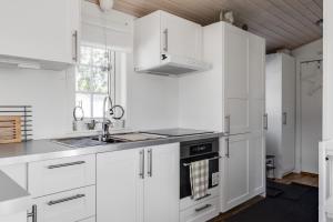 a white kitchen with white cabinets and a sink at Cozy mobile home near sandy beach in Hammar