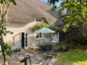 uma mesa com um guarda-chuva em frente a uma casa em Beautiful Character Thatched Pet Friendly House em Enford