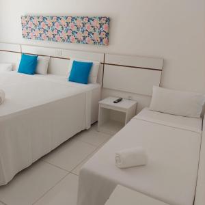 two beds with blue pillows in a white room at Aconchego Taperapuan Residencial Mont Carmelo in Porto Seguro