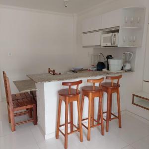 a kitchen with three wooden stools at a counter at Aconchego Taperapuan Residencial Mont Carmelo in Porto Seguro