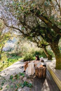 uma mulher sentada num banco debaixo de uma árvore em Cooking and Nature - Emotional Hotel em Alvados