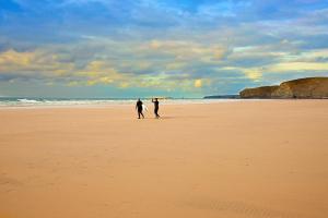 two people walking on a beach with a surfboard at Tregurrian Villas in Newquay