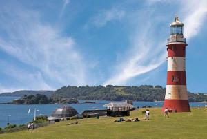 a red and white lighthouse in a grassy field next to the water at Barbican Boutique Luxury Apartments & Rooms, Plymouth in Plymouth