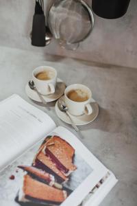 two cups of coffee and a piece of cake on a table at Rozenstein design residence in Brocēni