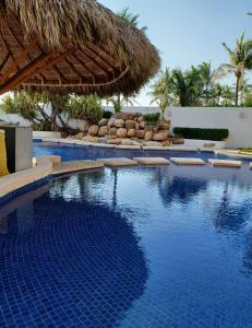 een zwembad met een rieten parasol en een resort bij Depa de lujo en Acapulco diamante sin daños por huracán Otis-Precio especial in Acapulco