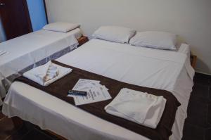 2 camas en una habitación con sábanas blancas y toallas en Pousada 76°, en Guarujá