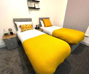 two beds with yellow and white sheets in a room at SA Stays in Wigan