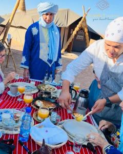 a group of people standing around a table with food at Pueblo Touareg - Private Tents in Merzouga