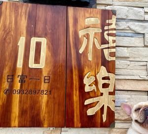 een hond die voor een houten bord met een bord zit bij 金門禧樂民宿 in Shan-ch'ien